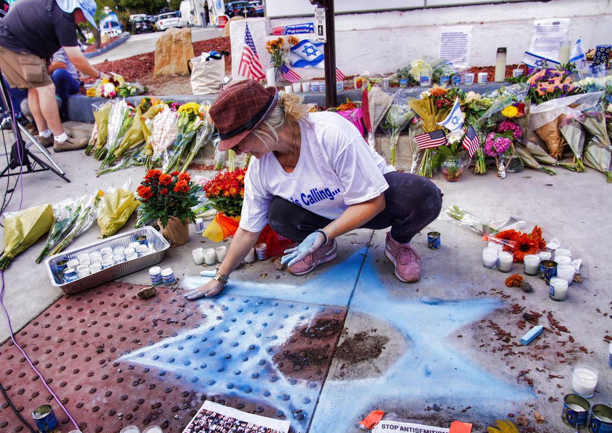  Elena Colombo chalks a Star of David amongst flowers and candles left at a makeshift memorial placed at the scene of a Nov. 5 confrontation that lead to death of a demonstrator in Thousand Oaks, Calif., on Nov. 7, 2023. (AP Photo/Richard Vogel)