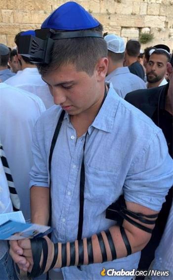 A college student dons tefillin at the Kotel.